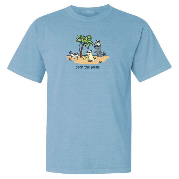 A light blue short-sleeve crewneck t-shirt featuring a cartoon graphic of dogs on a beach with palm trees and the text 'deck the palms' printed on the chest.