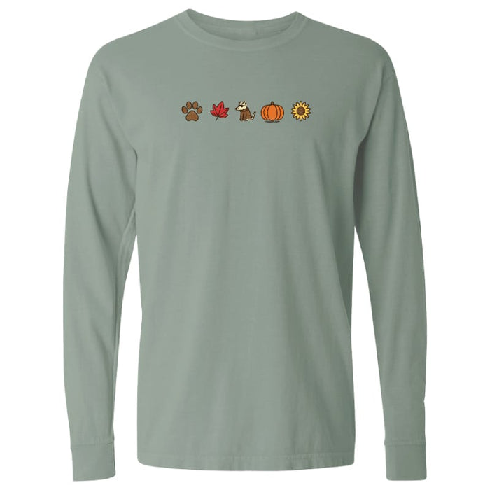A sage green long-sleeve t-shirt with a horizontal line of small autumn-themed icons printed across the chest, including a paw print, maple leaf, dog, pumpkin, and sunflower.