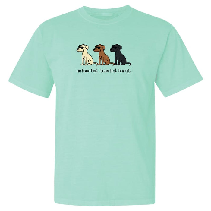A mint green short-sleeve t-shirt with a graphic of three cartoon dogs in cream, brown, and black, with the text 'untoasted. toasted.