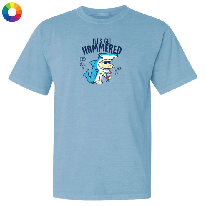 A light blue crewneck t-shirt featuring a cartoon graphic of a shark wearing sunglasses and a hammer, with the text 'LET'S GET HAMMERED' above it. A small multicolor color wheel icon is visible in the top-left corner.