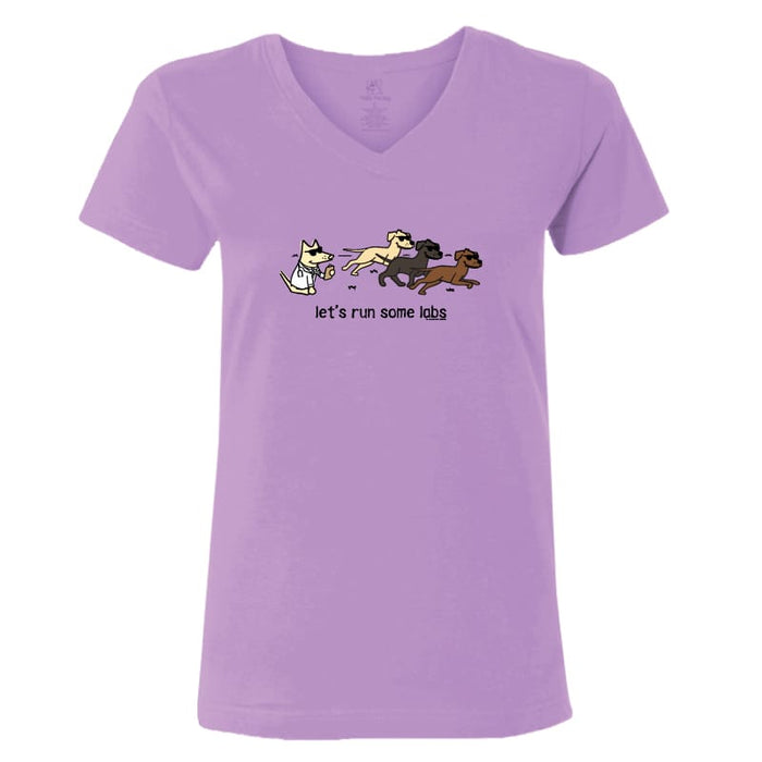 A light purple V-neck t-shirt featuring a cartoon graphic of a white cat chasing three running Labs, with the text 'let's run some labs' printed below.