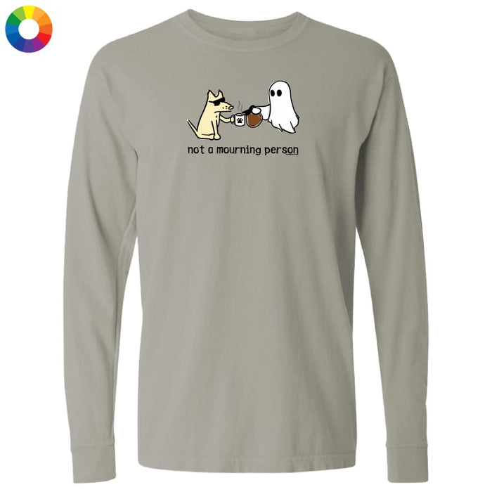 A light gray long-sleeve t-shirt with a cartoon graphic of a dog and a ghost playing coffee cups, with the text 'not a mourning person' printed below. A small multicolor color wheel icon is visible in the top-left corner.