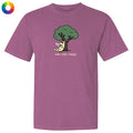 A mauve purple short-sleeve t-shirt with a cartoon graphic of a cat under a green tree reading 'read, relax, repeat.' on the chest, shown on a plain white background with a small multicolor color wheel icon in the top-left corner.