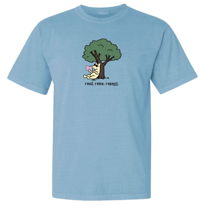 A light blue short-sleeve crewneck t-shirt featuring a cartoon graphic of a dog sitting under a tree reading a book, with the text 'read. relax.