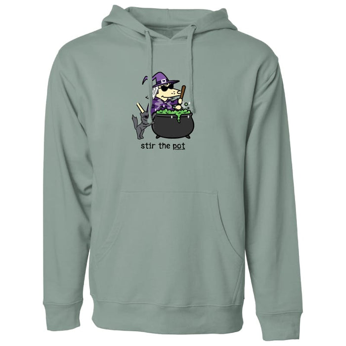 A sage green pullover hoodie with a cartoon graphic of a witch stirring a cauldron with the text 'stir the pot' printed on the chest.