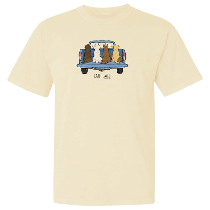 A cream-colored short-sleeve t-shirt with a graphic of four dogs sitting in the tailgate of a blue pickup truck, with the text 'TAIL-GATE' printed below.