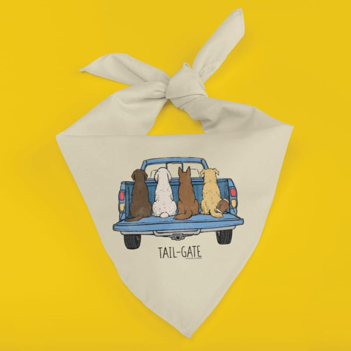 An off-white cotton bandana dog collar with a printed graphic of four dogs sitting in the back of a blue pickup truck, labeled 'TAIL-GATE', set against a solid bright yellow background.