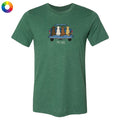 A green heathered short-sleeve t-shirt with a graphic of four dogs sitting in the back of a pickup truck, with the text 'TAIL-WIT' below. A small multicolor color wheel icon is in the top-left corner, set against a plain white background.